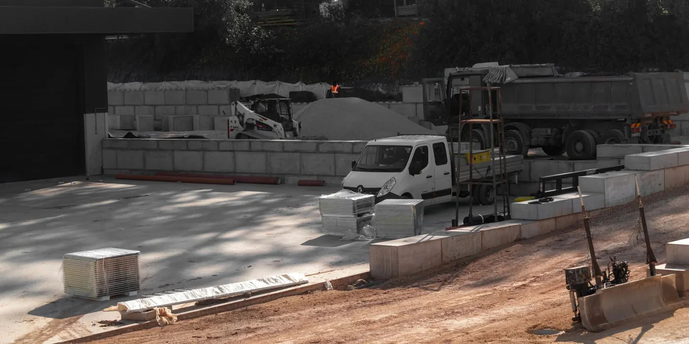 Building site with a pile of gravel, a skid steer, a dump truck and stacked concrete blocks