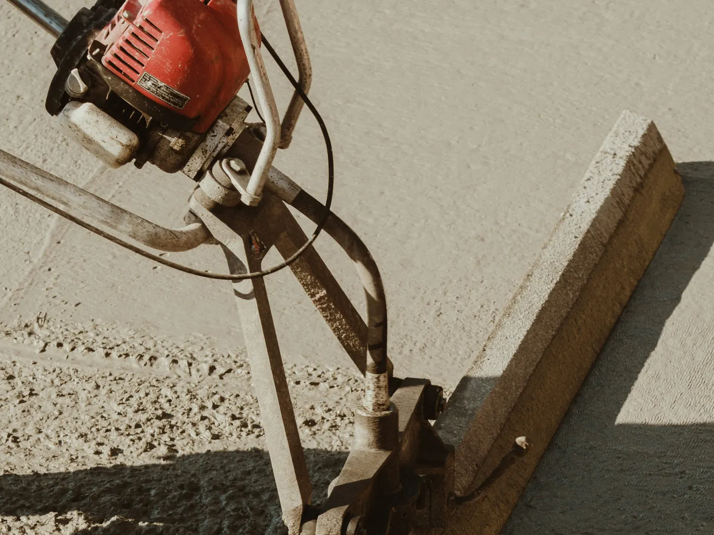 A gas-powered screed with a red engine leveling fresh concrete