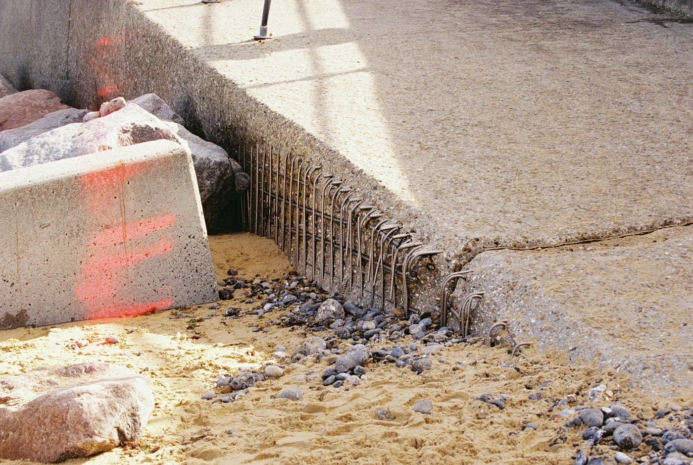 Concrete edge with the sand washed out from beneath it, exposing a row of bent steel reinforcing bars